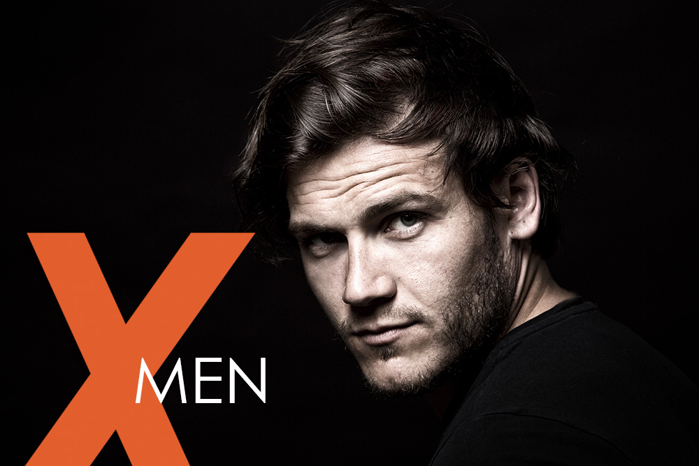 Stimmungsvolles Porträt eines Mannes mit Bart und dunklem Haar auf schwarzem Hintergrund – Symbolbild der NEOVITA MEN Pflegeserie für kraftvolle, moderne Männerpflege mit dem markanten orangefarbenen „X“-Design.